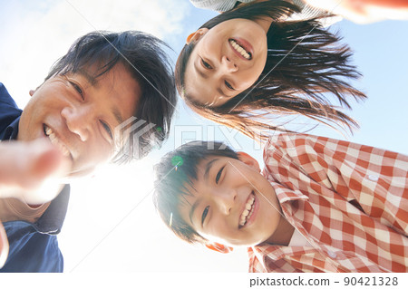 A family of three looking into the camera with a smile under the blue sky A family of three looking into the camera with a smile under the blue sky 90421328