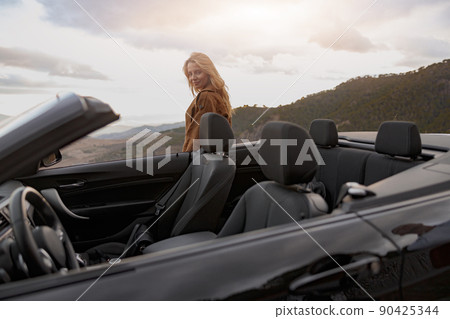 Pretty Caucasian young happy female standing outdoor behind convertible car looking at camera  90425344