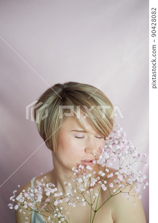 Portrait of a girl on a pink background with flowers. Tenderness and feminine. The sphere of beauty and women's health. Short haircut, blonde hair 90428082