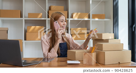 Young Asian small business owner working at home office, taking note on purchase orders. Online marketing packaging delivery, startup SME entrepreneur or freelance woman concept 90428625