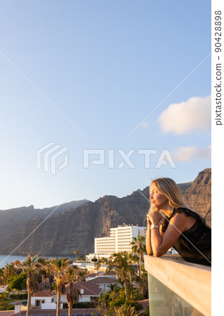 Young woman on a balcony enjoying view to the cliffs and ocean. 90428898