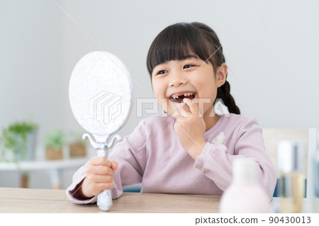 Elementary school girl looking at teeth missing in the mirror 90430013