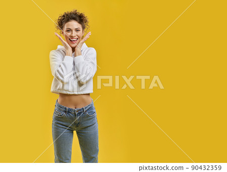 Excited woman, putting hands to face in admiration, looking at camera with smile inside. Portrait view of surprised cute girl, enjoying, isolated on orange studio background. Concept of emotions. 90432359