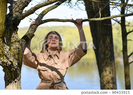 Girl in a jacket near a tree in the forest near the lake Girl in a jacket near a tree in the forest near the lake 90433915
