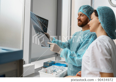 Doctor and nurse in uniform look and discuss an X-ray or MRI scan of the patient spine Doctor and nurse in uniform look and discuss an X-ray or MRI scan of the patient spine 90434972