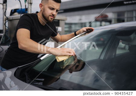 Man wipes a windshield of his car with a rag in a showroom at a self-service car wash Man wipes a windshield of his car with a rag in a showroom at a self-service car wash 90435427