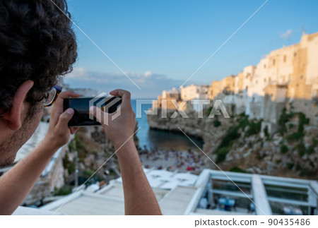 Polignano a mare, Puglia, Italy. August 2021. A young man with curly hair and glasses admires the view of Cala Monachile Polignano a mare, Puglia, Italy. August 2021. A young man with curly hair and glasses admires the view of Cala Monachile 90435486
