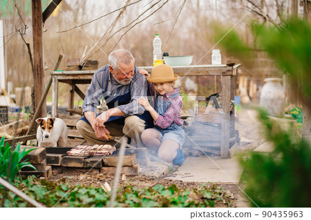 granddaughter helps grandfather with dog cook barbecue on the grill, bonfire 90435963