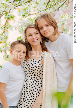 a happy and beautiful mother of two teenage sons in a blooming spring garden.  90435967