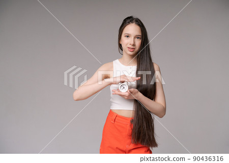 Young girl holding small alarm clock in her hands in casual clothes posing 90436316