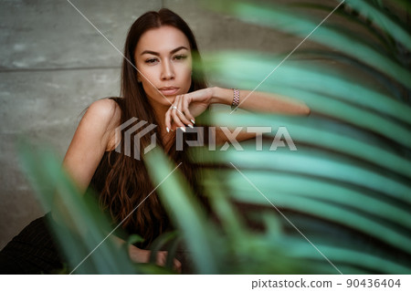 Woman portrait on a background of a gray wall through the leaves of a flower Woman portrait on a background of a gray wall through the leaves of a flower 90436404