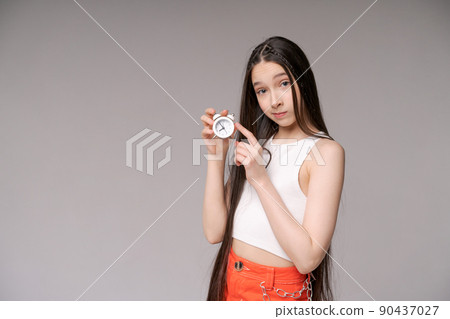 Young girl holding small alarm clock in her hands in casual clothes posing 90437027