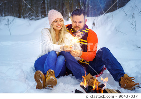 Happy couple in winter in the forest by the fire with sparklers 90437037