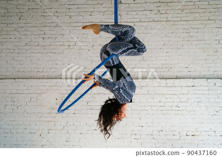 Young woman is engaged in aerial acrobatics on a white brick background. 90437160
