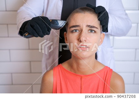 Young woman is forcibly shaving her head with an electric razor, holding 90437208