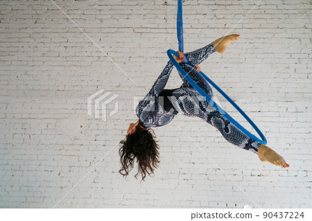 Young woman is engaged in aerial acrobatics on a white brick background. Young woman is engaged in aerial acrobatics on a white brick background. 90437224