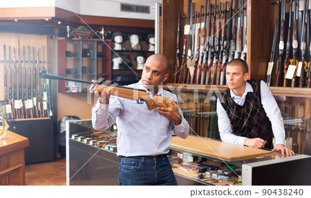 Hispanic man examining break-barrel air rifle in gunsmith store Hispanic man examining break-barrel air rifle in gunsmith store 90438240