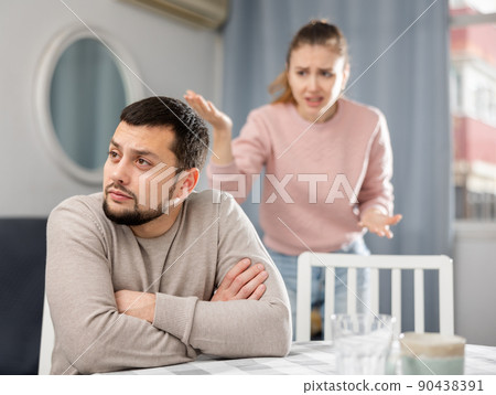 Man sitting at table during quarrel with his wife Man sitting at table during quarrel with his wife 90438391
