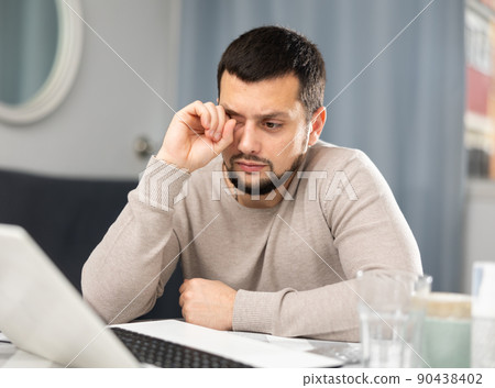 Young man suffering from eye pain after work on laptop at home Young man suffering from eye pain after work on laptop at home 90438402