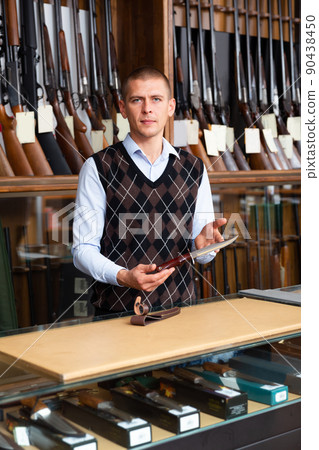 Gunsmith shop assistant demonstrates hunting knife in hands Gunsmith shop assistant demonstrates hunting knife in hands 90438450