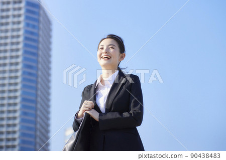 Young woman in a recruitment suit, blue sky, skyscraper, smile 90438483