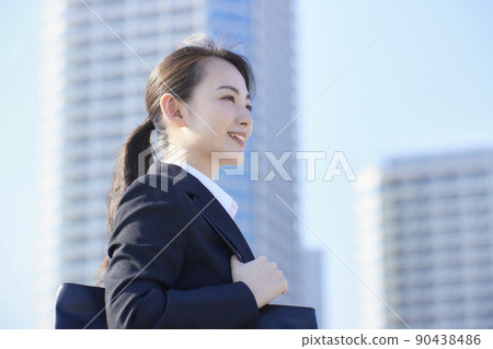 Young woman in a recruitment suit, blue sky, skyscraper, smile 90438486