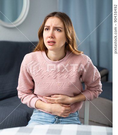 Young woman suffering from stomach pain at home Young woman suffering from stomach pain at home 90438492