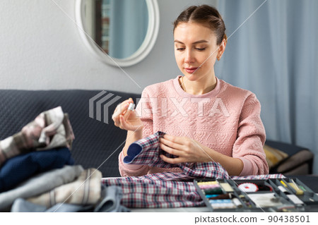 Young woman sewing on button at home Young woman sewing on button at home 90438501