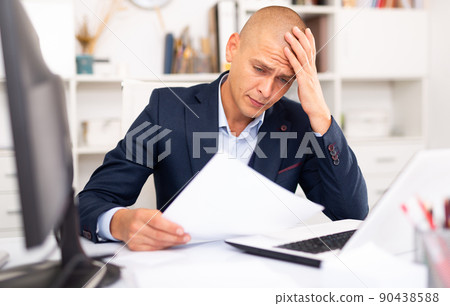 Upset young businessman working documents and laptop 90438588