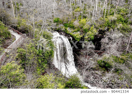 A scenic waterfall roadside going over the cliff down to the boulders and rocks below where you can no longer drive under but can walk underneath the raging waters 90441334