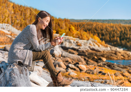 Mobile phone travel lifestyle Asian woman using cellphone data durig outdoor hiking adventure in Quebec, Canada. Happy girl texting in forest autumn foliage. Technology Mobile phone travel lifestyle Asian woman using cellphone data durig outdoor hiking adventure in Quebec, Canada. Happy girl texting in forest autumn foliage. Technology 90447284