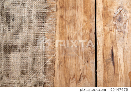 The burlap lies on the tabletop of a wooden table. Rough cloth on top of rough boards. Top view The burlap lies on the tabletop of a wooden table. Rough cloth on top of rough boards. Top view 90447476