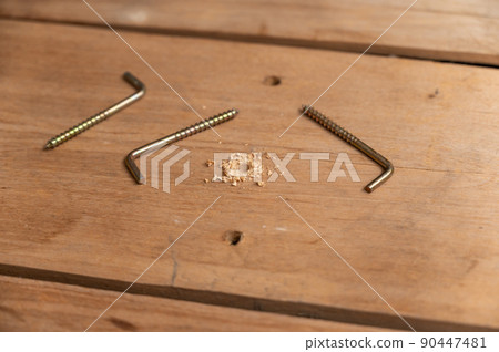 L-hook screws lie on wooden planks. Three plated screws. Drilled hole in the board. Selective focus. L-hook screws lie on wooden planks. Three plated screws. Drilled hole in the board. Selective focus. 90447481