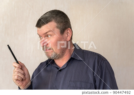 Portrait of a grown man gesturing with a pencil in his hand. A man with a short haircut and graying hair. Looking away. Indoors. 90447492