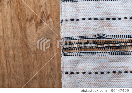 A white kitchen towel lies on the countertop of a wooden table. The fringed towel is fringed and patterned on the rough boards. Top view. Copy space A white kitchen towel lies on the countertop of a wooden table. The fringed towel is fringed and patterned on the rough boards. Top view. Copy space 90447499