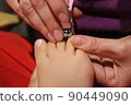 The master covers the customer's nails with varnish. Hands in gloves cares about a woman's foot nails. Pedicure, manicure beauty salon concept. Nail varnishing in red color. 90449090