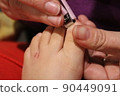 The master covers the customer's nails with varnish. Hands in gloves cares about a woman's foot nails. Pedicure, manicure beauty salon concept. Nail varnishing in red color. 90449091