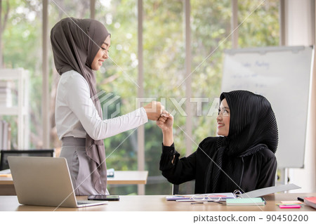 Smart and beautiful Asian muslim business people expressing happy emotion together in meeting room. Muslim business woman making hand shake to her colleague. Business deal and discussion concept. Smart and beautiful Asian muslim business people expressing happy emotion together in meeting room. Muslim business woman making hand shake to her colleague. Business deal and discussion concept. 90450200