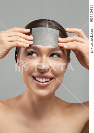 Skin care. Young woman removing oil from face using blotting papers. Beautiful girl model with smooth and healthy skin. 90450455