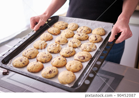 Woman holding baking tray full of freshly made Chocolate chip cookies 90452087