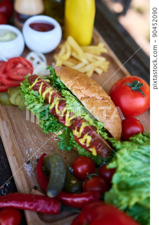 BBQ hot dog served with vegetables and French fries and sauces on wooden serving board 90452090
