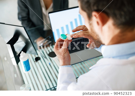 Male optometrist hands giving pair of contact lens in case to patient offering choice Male optometrist hands giving pair of contact lens in case to patient offering choice 90452323