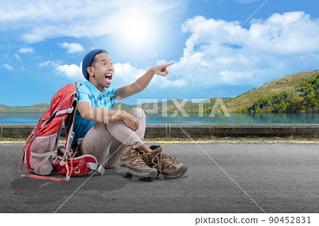 An Asian man with a beanie hat and a backpack sitting and pointing at something on the street An Asian man with a beanie hat and a backpack sitting and pointing at something on the street 90452831