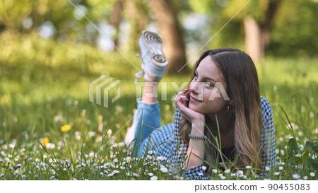 The girl lies in the grass between flowers. 90455083