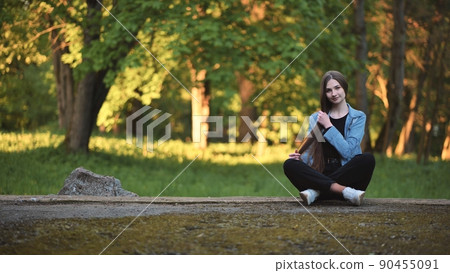A young girl strokes her long hair while sitting in the park. 90455091