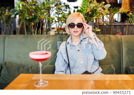 Portrait of attractive young woman drinking coctail in cafe indoor. Beautiful blonde woman relaxing at the bar and drinking a cocktail Portrait of attractive young woman drinking coctail in cafe indoor. Beautiful blonde woman relaxing at the bar and drinking a cocktail 90455271