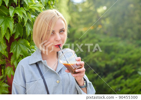 Stylish young blonde walks around the city and drinks a cold drink. Stylish young blonde walks around the city and drinks a cold drink. 90455300