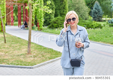 Stylish young blonde walks around the city and drinks a cold drink and talks on the phone. Stylish young blonde walks around the city and drinks a cold drink and talks on the phone. 90455301