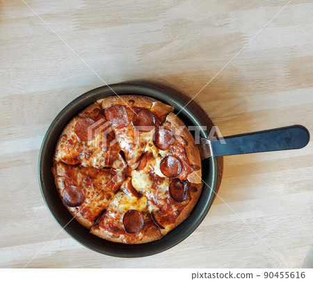 Top view of Italian salami pizza with mozzarella and herb on a black pan on brown wood table Top view of Italian salami pizza with mozzarella and herb on a black pan on brown wood table 90455616
