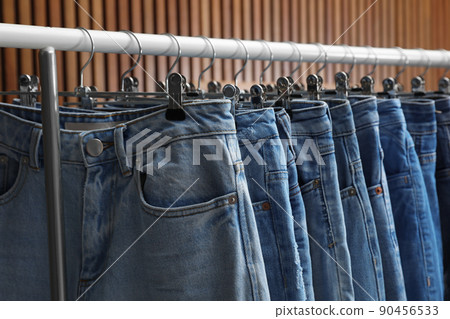 Rack with different jeans on wooden background, closeup 90456533